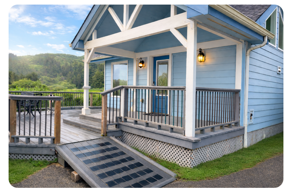 Blue house porch with wooden railings, steps, and a ramp in a grassy rural setting