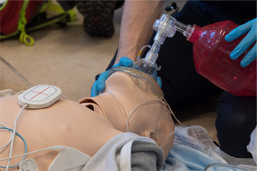 A person is putting an oxygen mask on an ACLS Manikin 