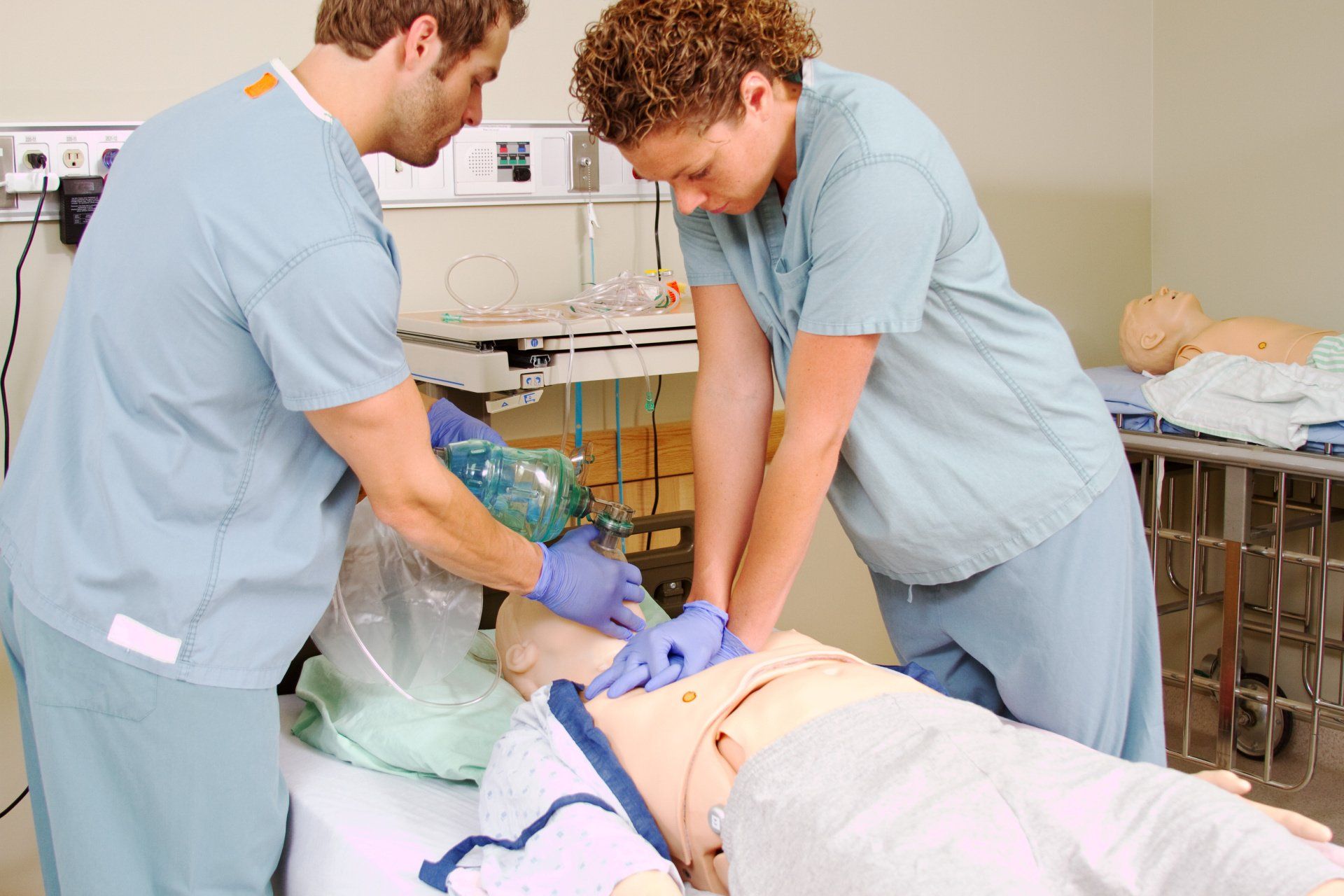 two nurses are practicing on a mannequin in a hospital room