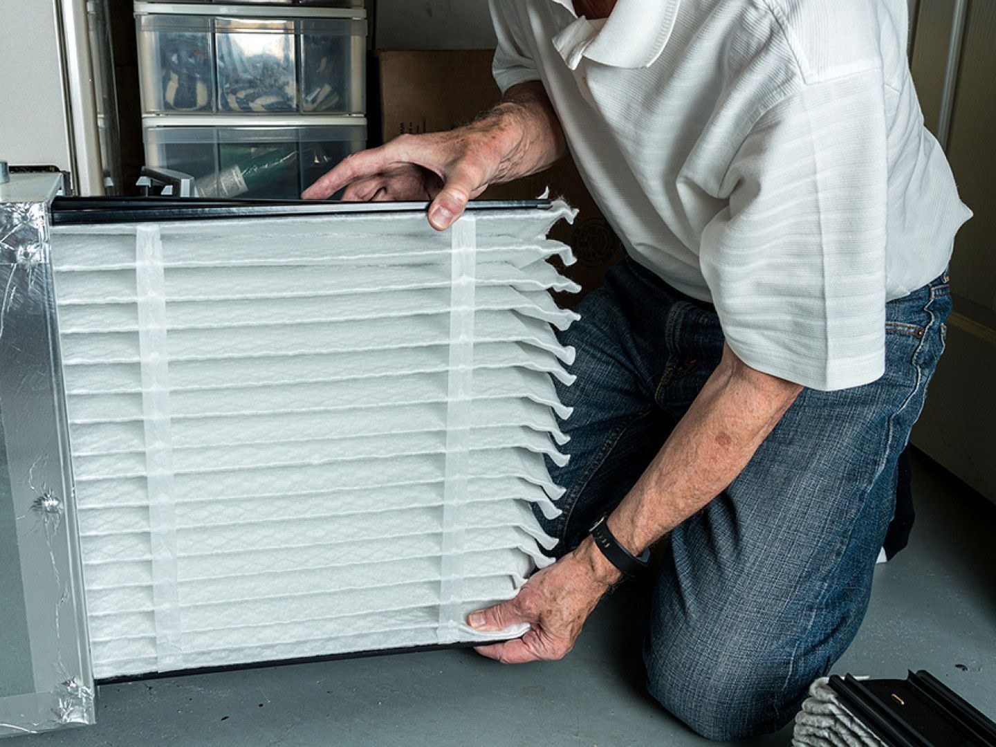 A man is kneeling down in front of a large air filter.