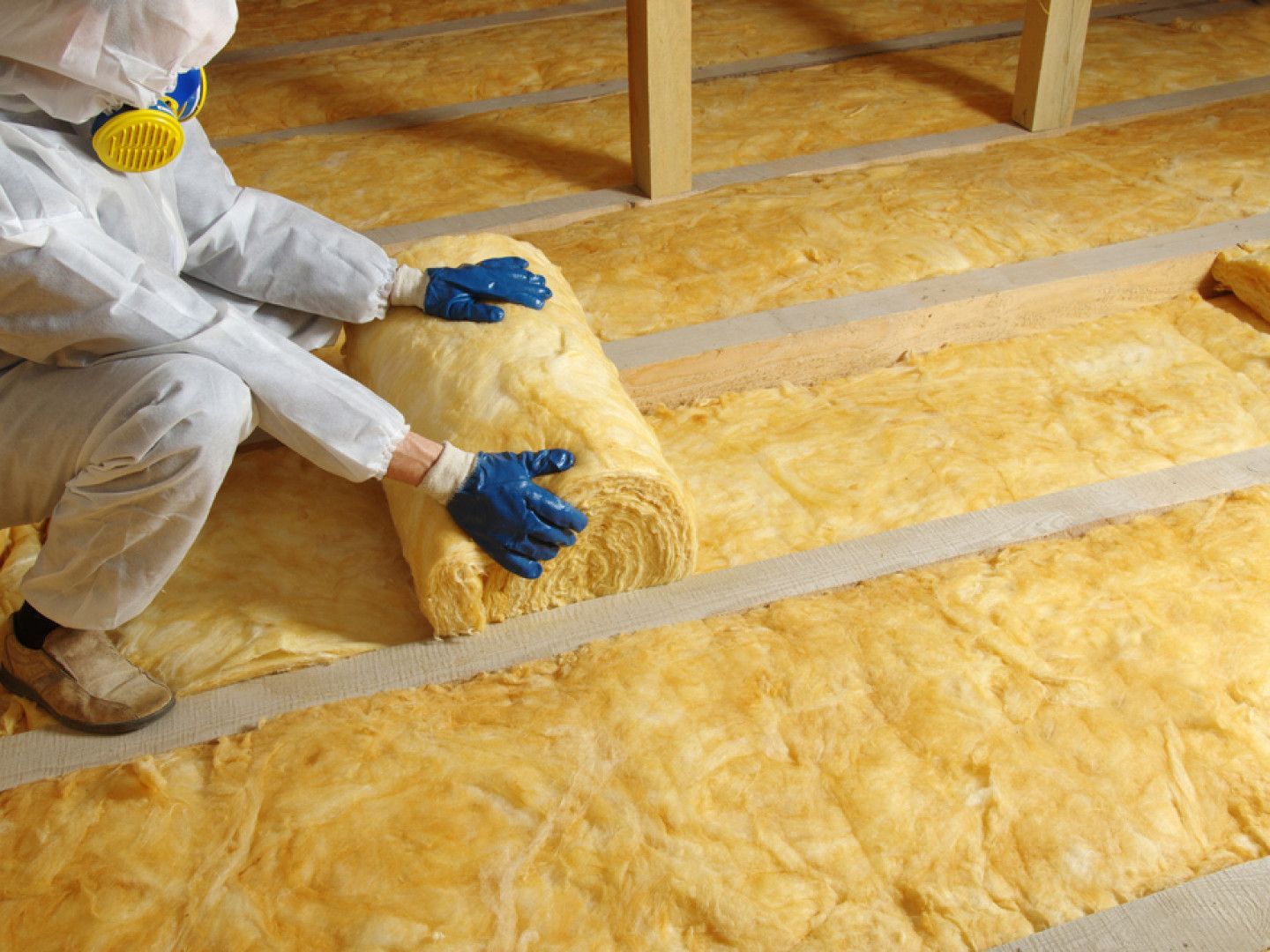 A person is kneeling on a roll of insulation on the floor.