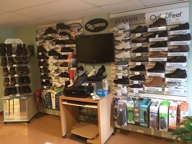 Shoe store interior with display walls showcasing various shoe styles and brands. A TV, desk, and accessories are visible.