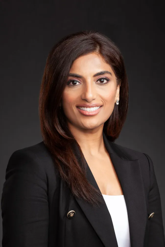 Woman in black blazer, smiling at the camera, against a dark gray background.