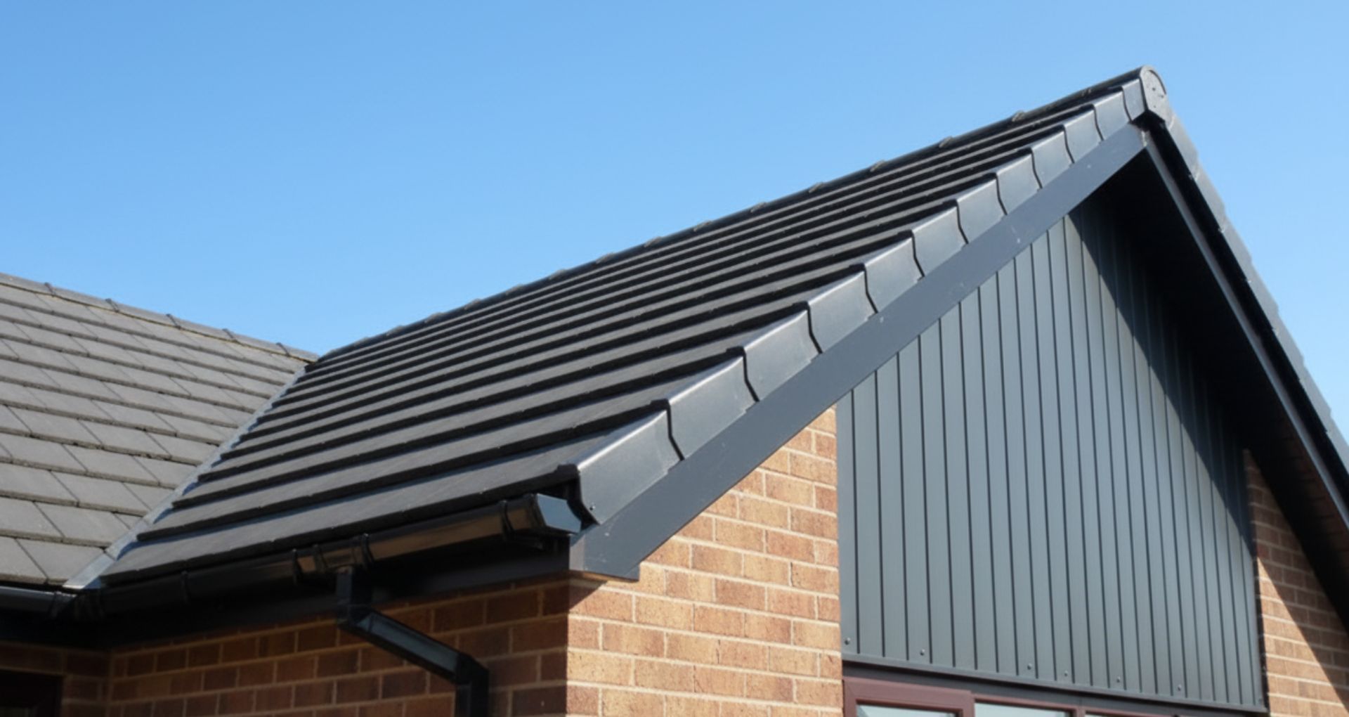 A brick building with a dark tiled roof and black trim against a clear blue sky.