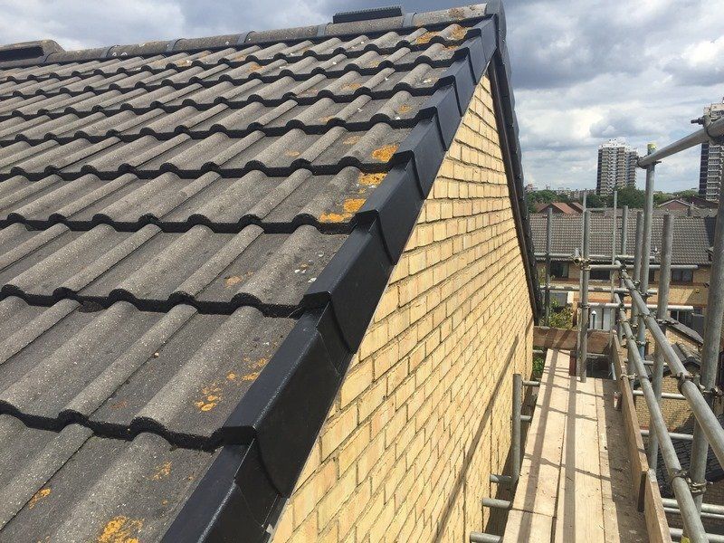 Roof with gray tiles and black edging, adjacent to a yellow brick wall and scaffolding.