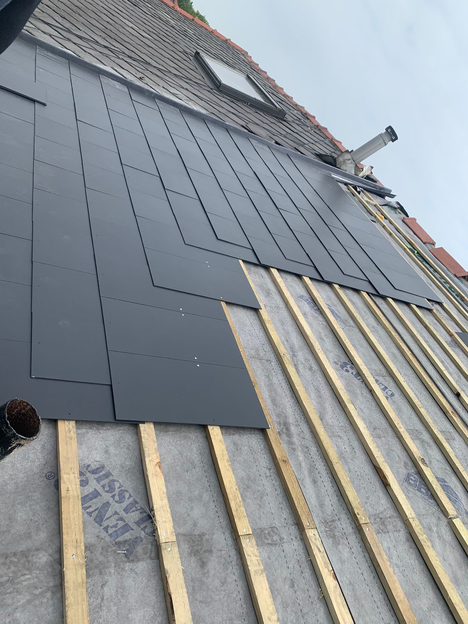 Roof in progress with dark gray panels being installed on wooden rafters.