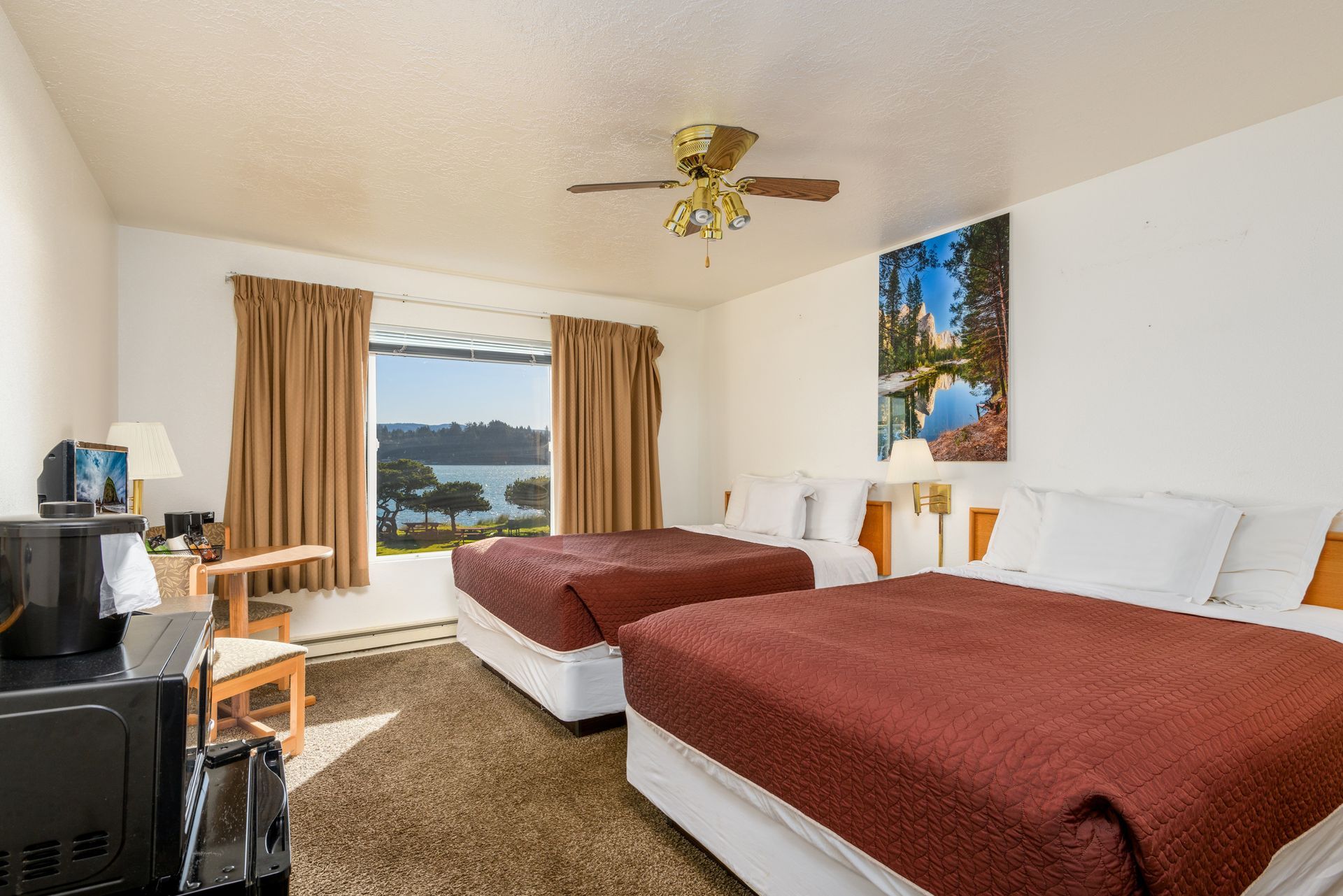 Hotel room with two beds, window with a water view, and a mounted landscape painting.