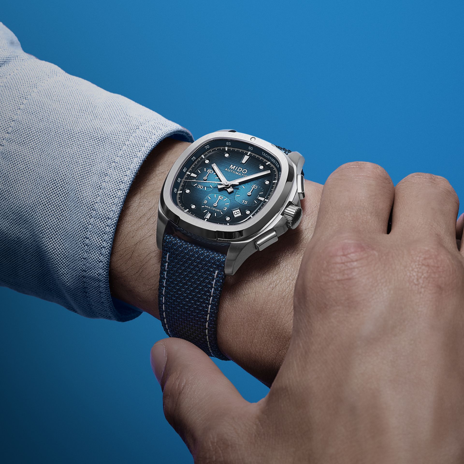 Primo piano di un orologio da polso al polso di una persona, su sfondo blu.