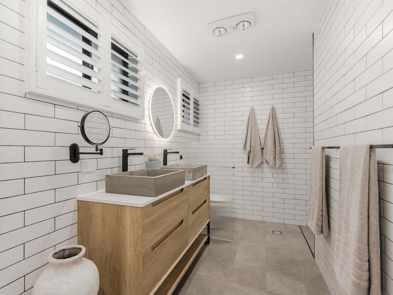 A bathroom with white brick walls , a sink , a mirror and a vase.