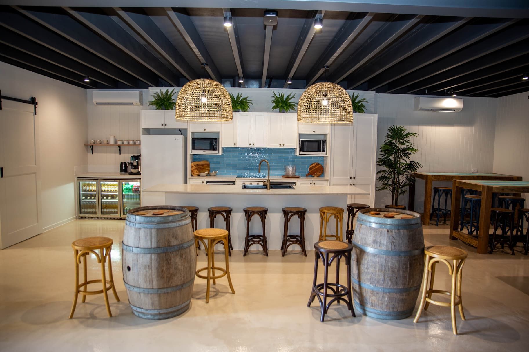 barrels and stools in the middle of the room in front of a kitchen with lights above