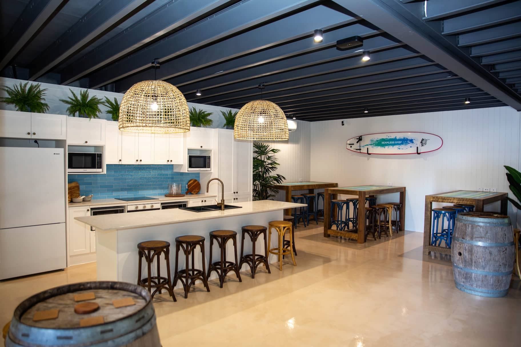 Modern kitchen area with a white island, seating, and a surfboard on the wall.
