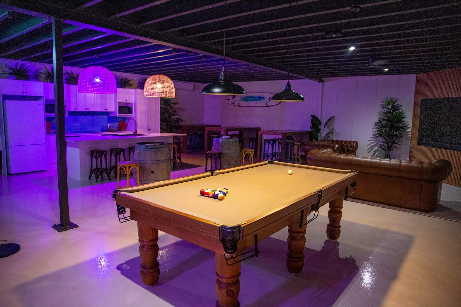 A pool table in the middle of the room with coloured lights in the background.