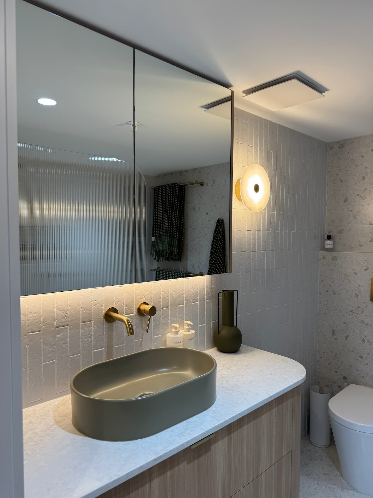 Modern bathroom with gray oval sink, gold faucet, and textured wall tiles.