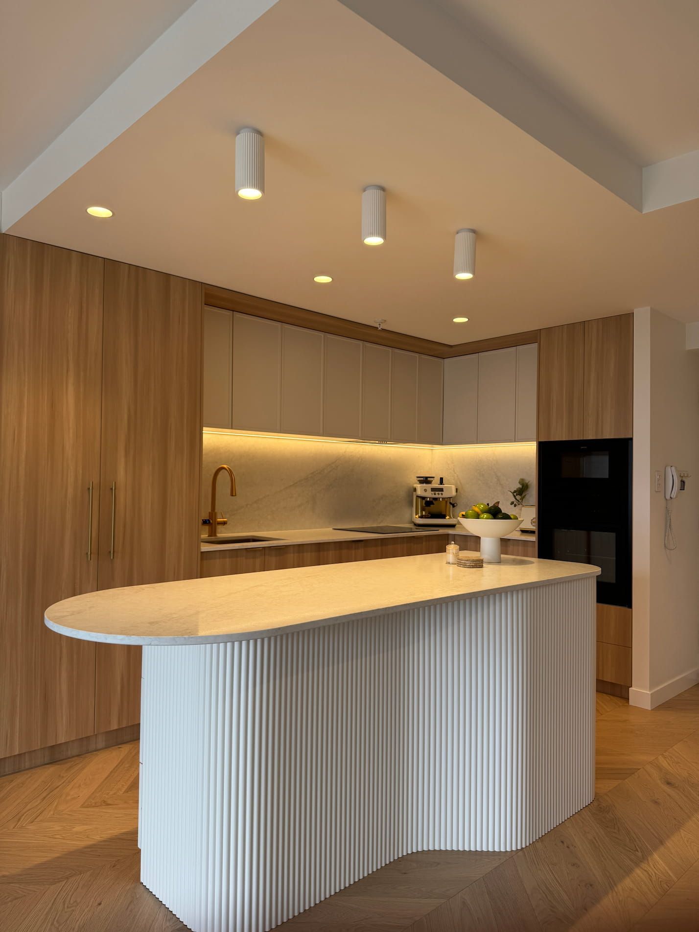 Modern kitchen with light wood cabinets, white island, and recessed lighting.