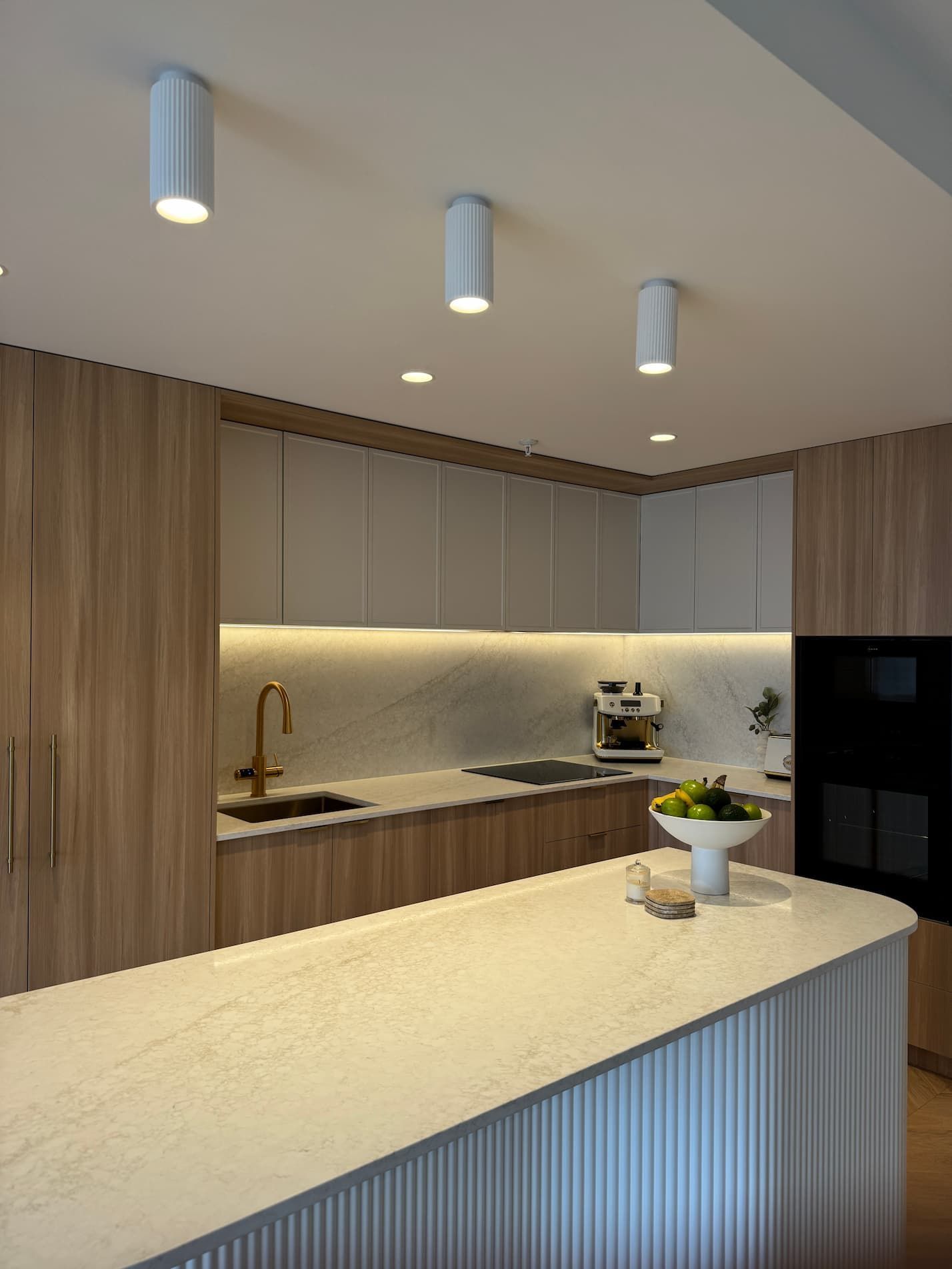 Modern kitchen with light wood cabinets, white countertops, and recessed lighting.