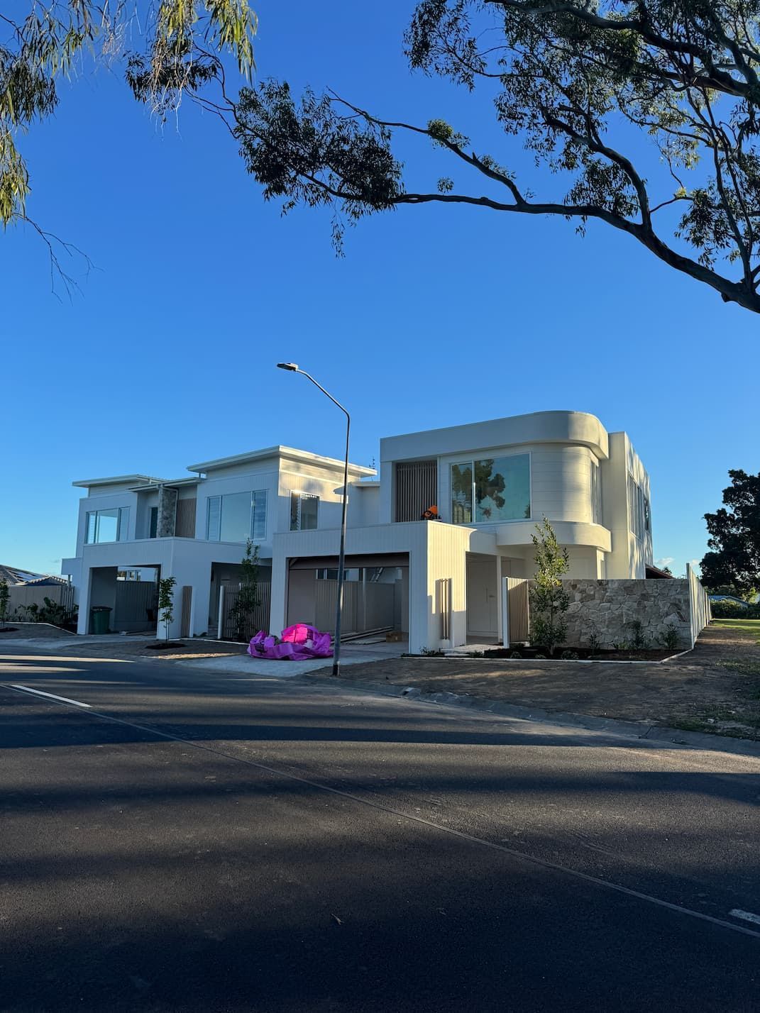 Modern, light-colored houses under construction, set against a blue sky, with some tree branches in the foreground.