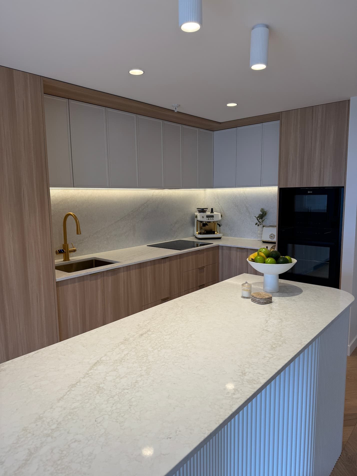 Modern kitchen with light wood and gray cabinets, island, and built-in oven.