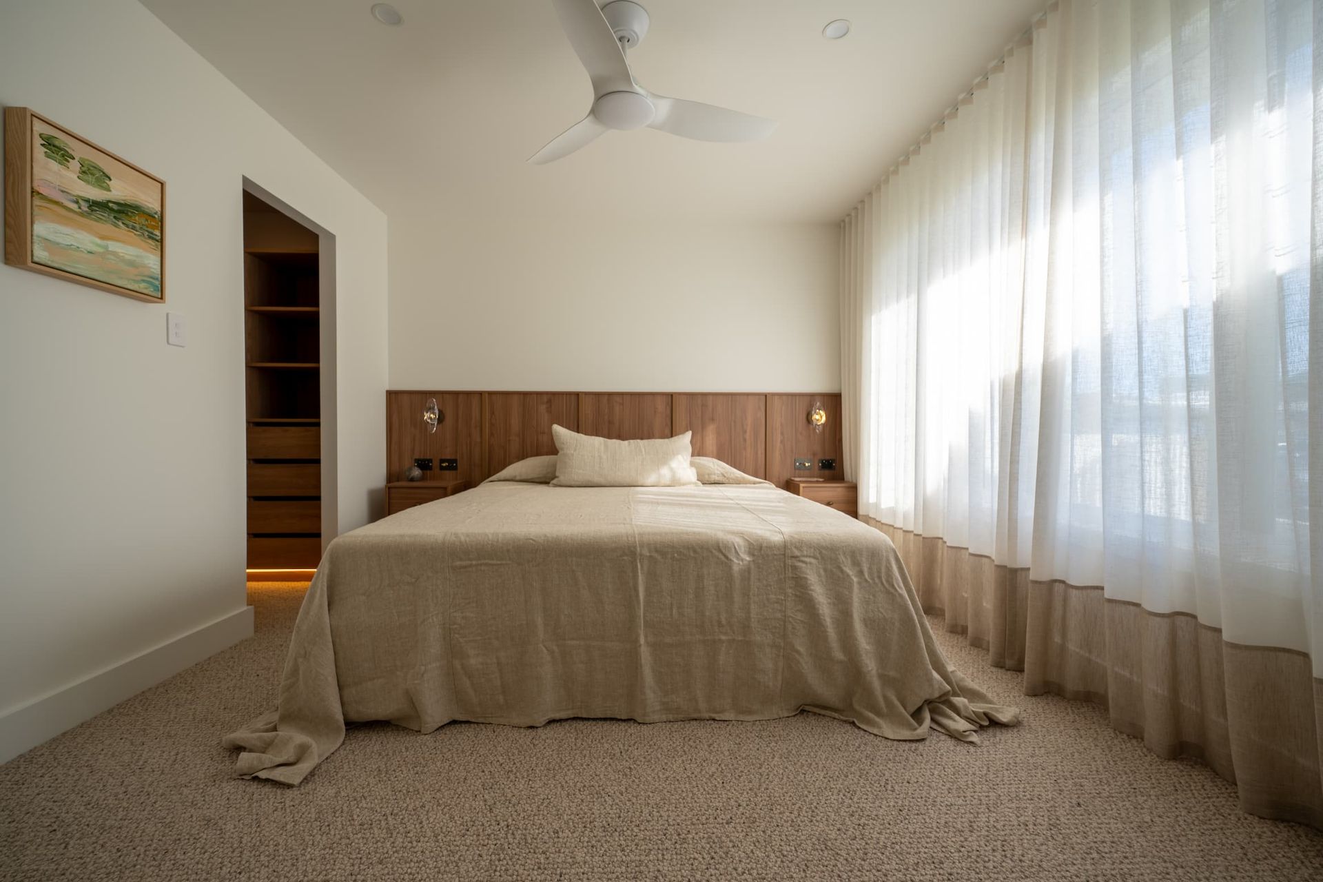 Bedroom with bed, closet, art, and sheer curtains. Light brown and white tones.