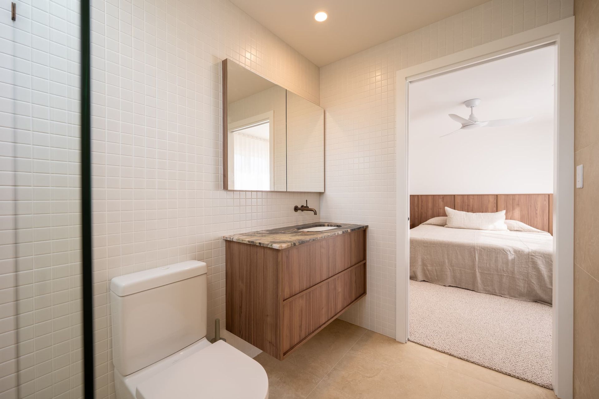 Bathroom with a toilet, floating vanity, and a bedroom visible through the doorway.