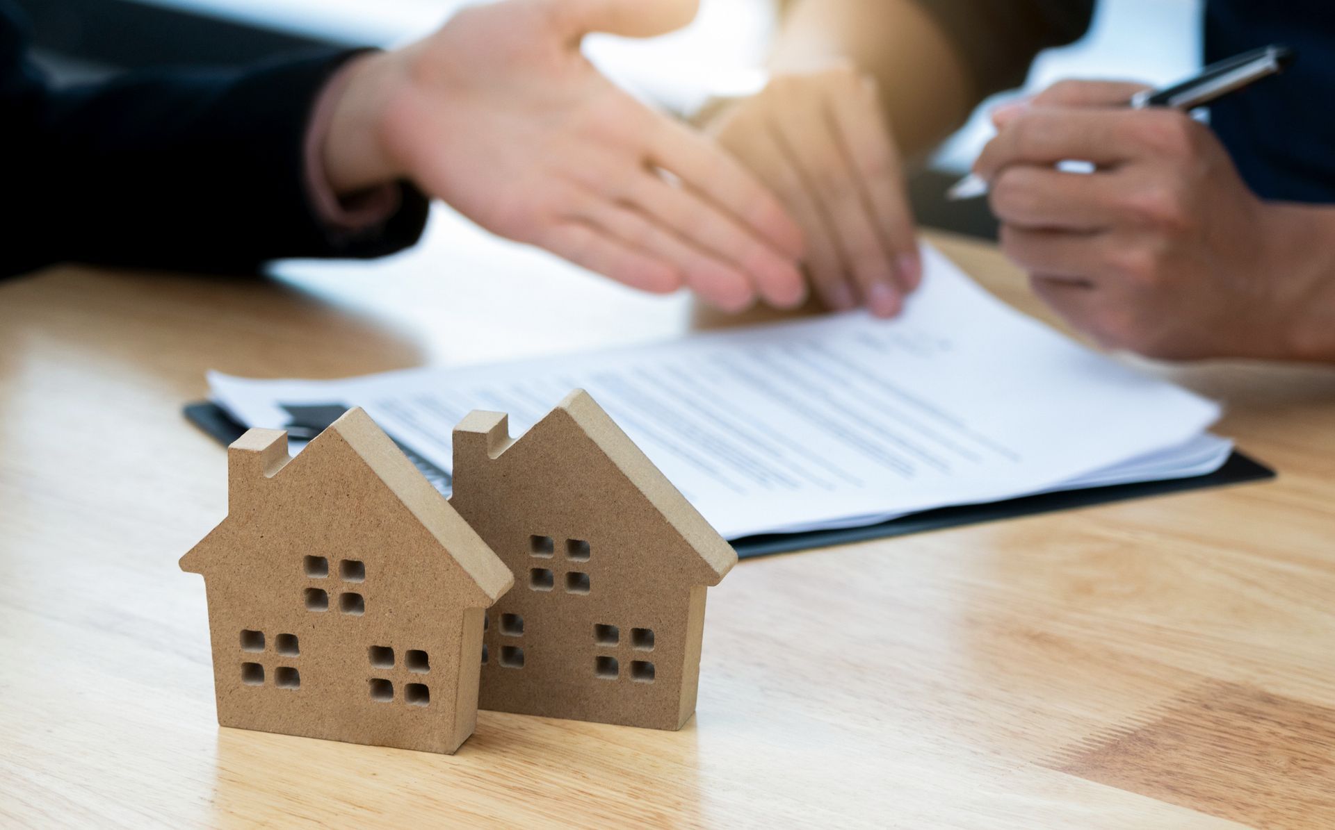 Two people discussing a contract with small wooden house models on the table.