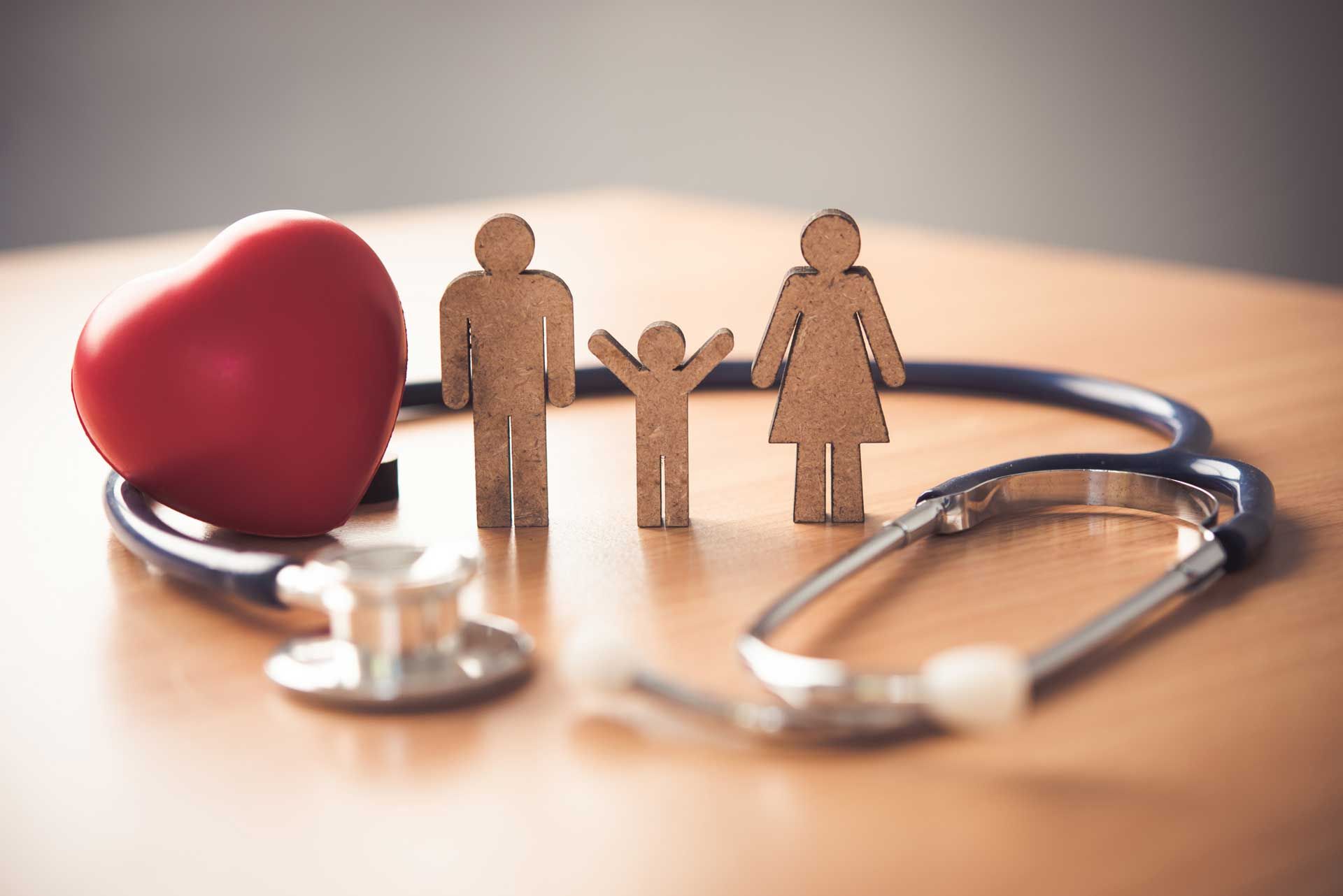 A wooden family , a stethoscope , and a heart are on a wooden table.