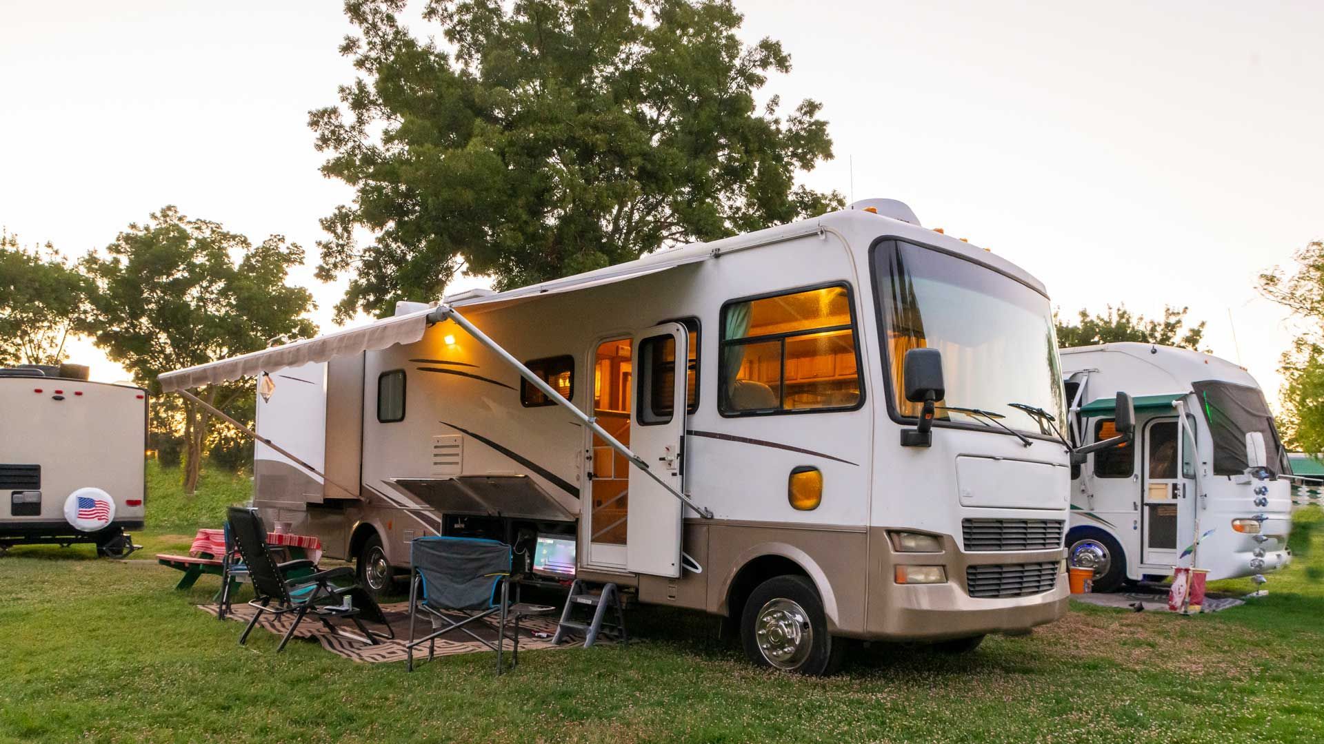 A rv is parked in a grassy field next to another rv.