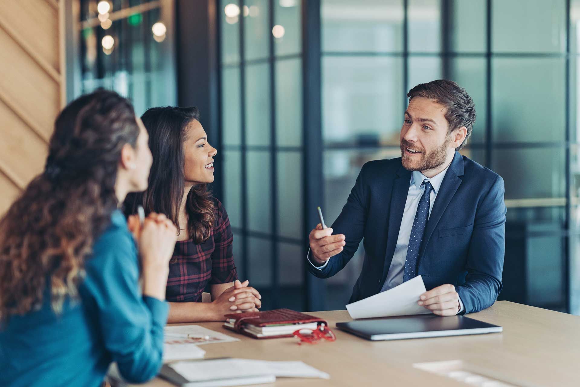 A man in a suit and tie is sitting at a table talking to two women.