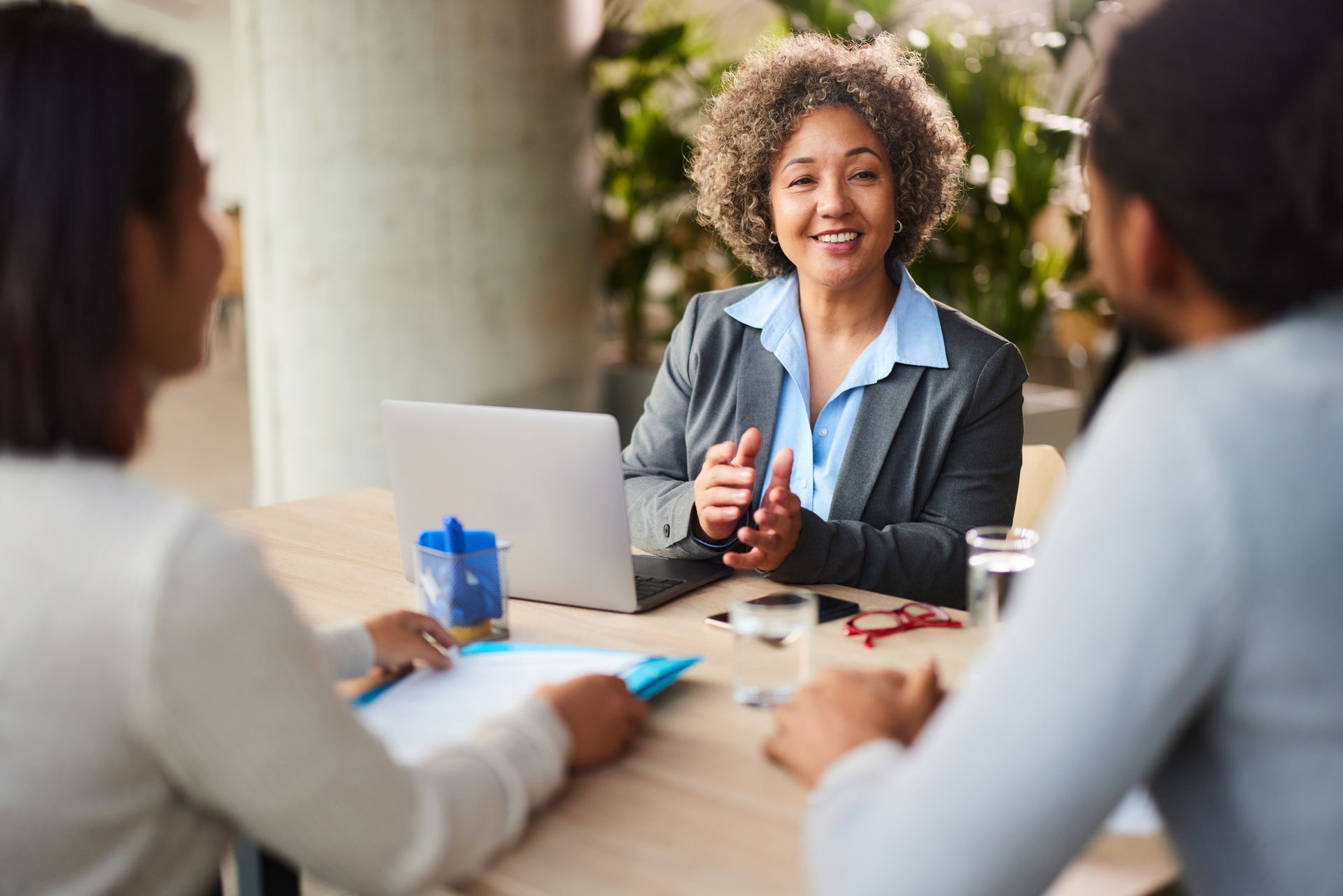 A happy insurance agent working on a computer while talking to her customers during a meeting A happy insurance agent working on a computer while talking to her customers during a meeting