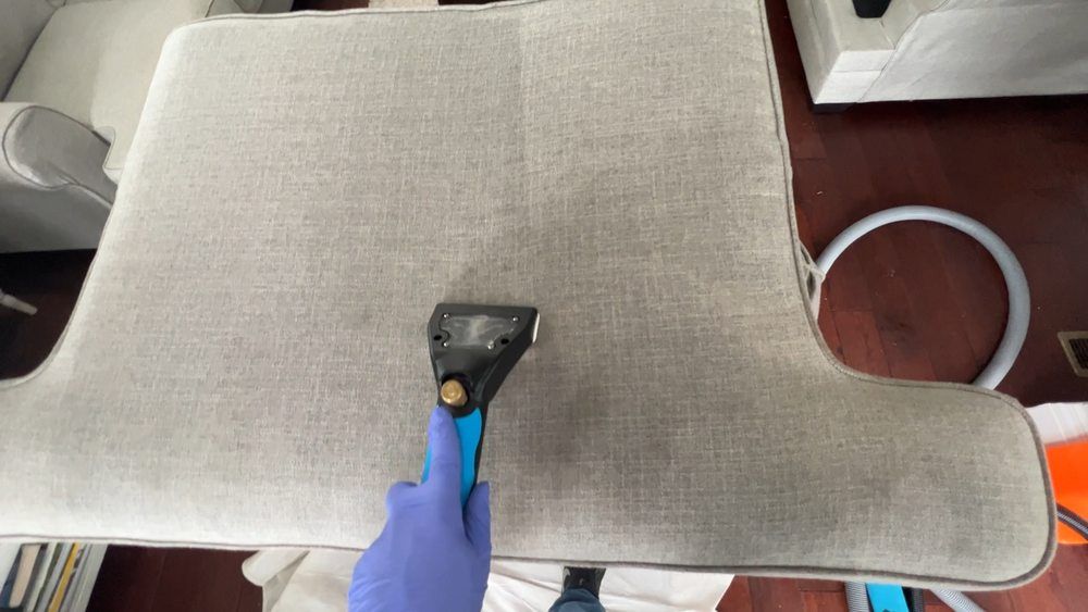 A person is cleaning a couch with a vacuum cleaner.