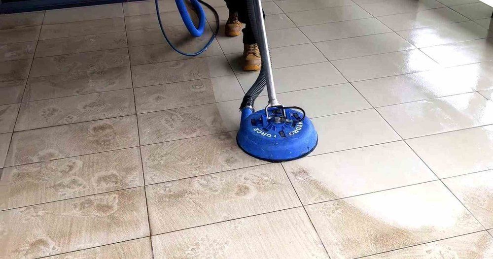 A person is cleaning a tiled floor with a vacuum cleaner.