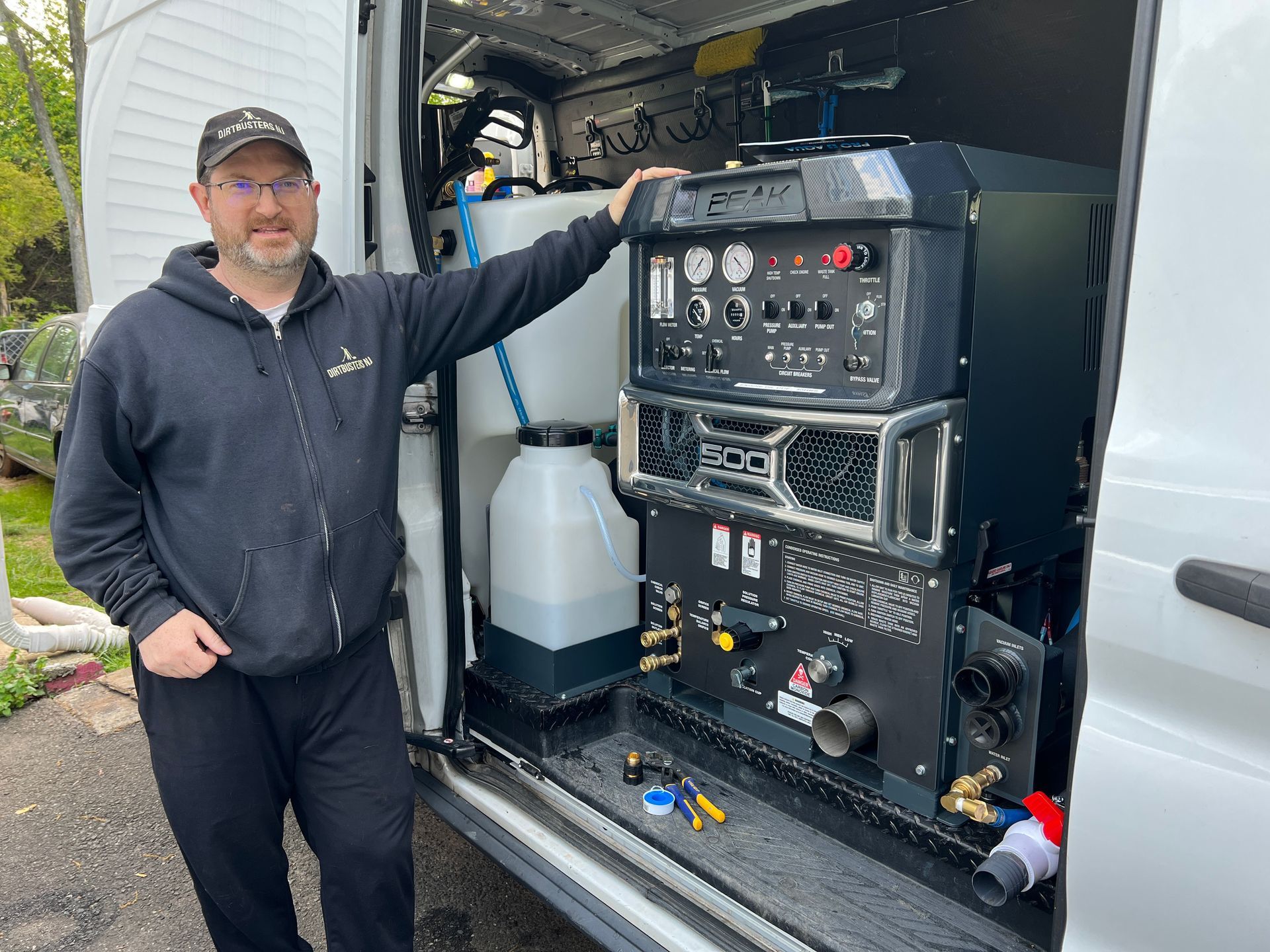 A man is standing in front of a van with a machine in the back.