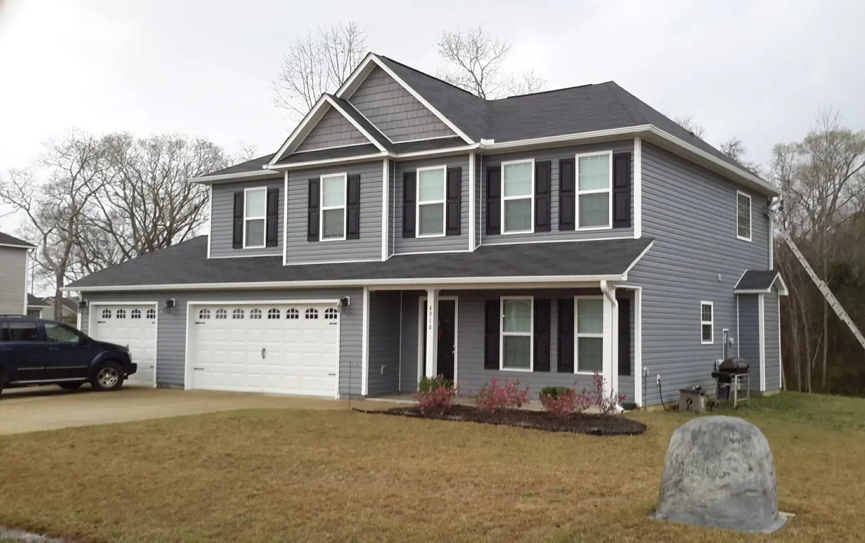 Two-story gray house with white trim, a porch, and a two-car garage on a sunny day.