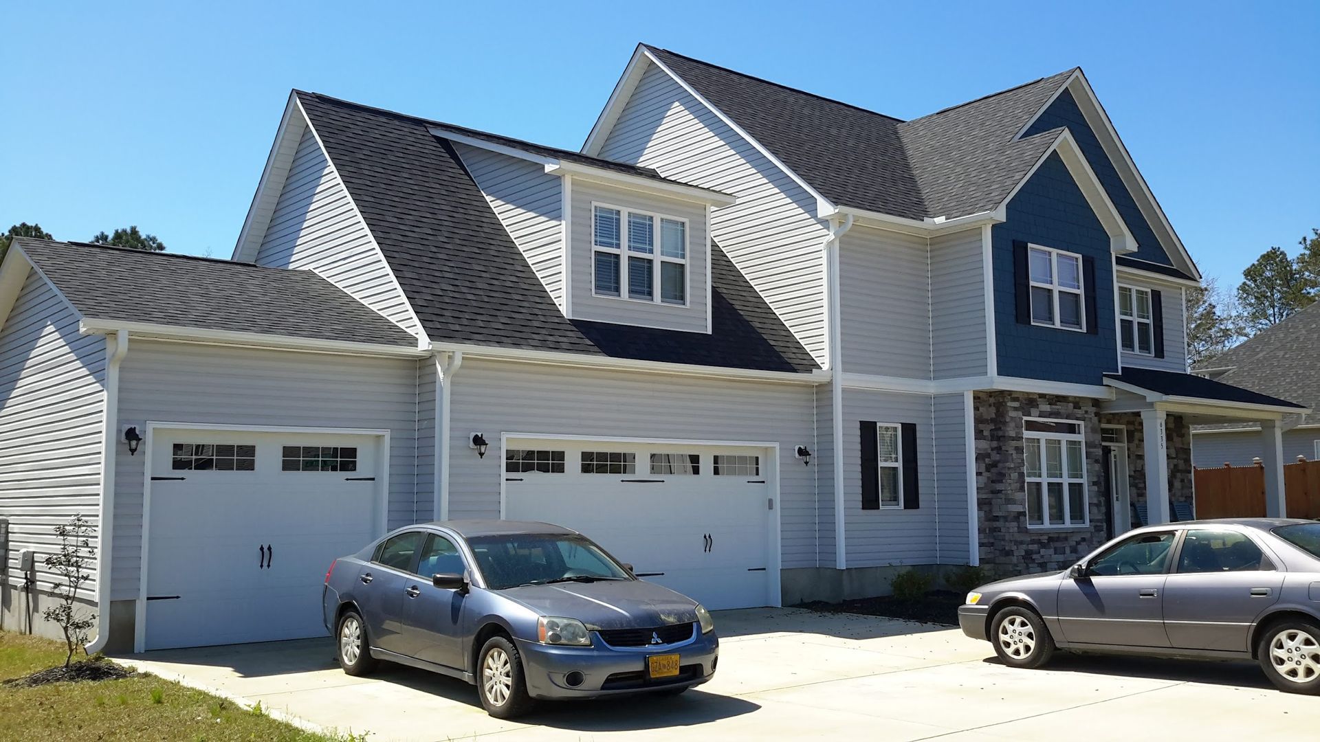 Two-story modern house with beige siding, brown trim, and a two-car garage, in front of a blue sky.