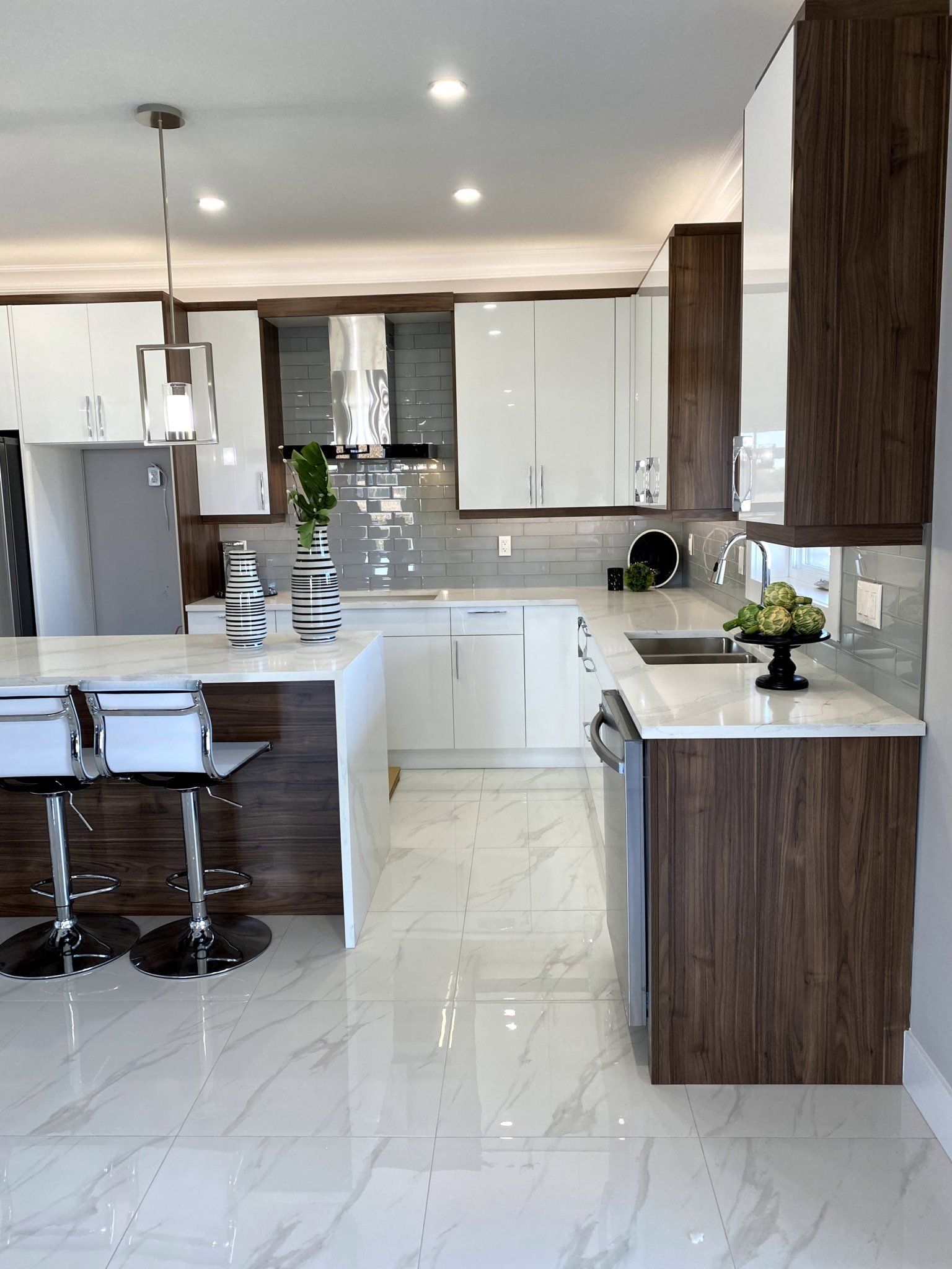 Modern kitchen with white and wood cabinets, light-colored countertops, stainless steel appliances, and a marble floor.