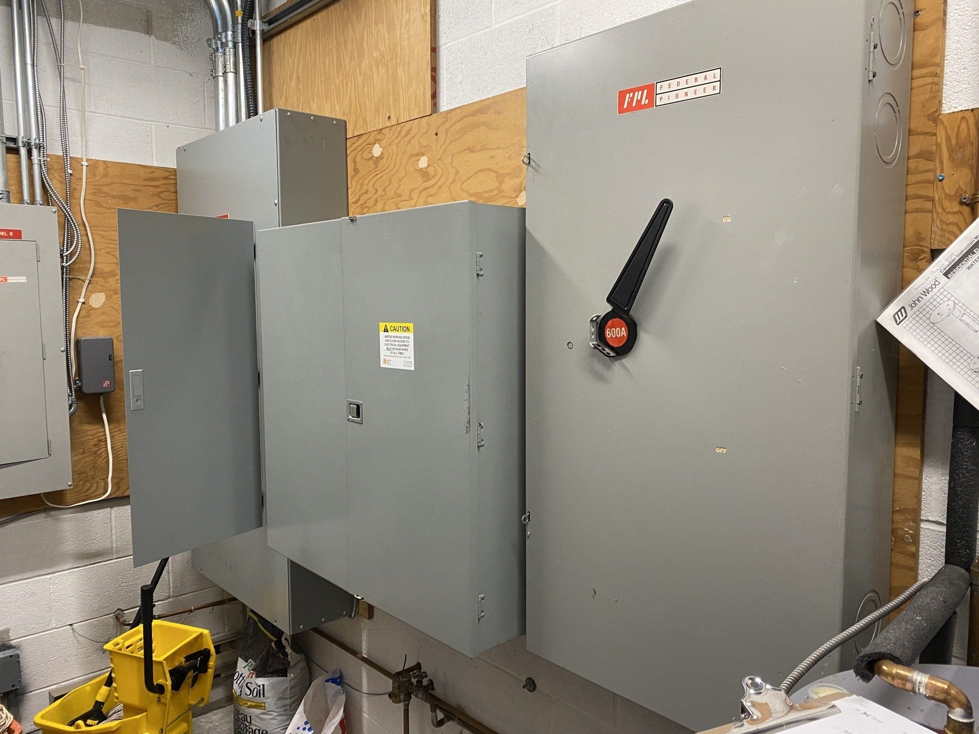 Gray electrical panel with large black switch on a plywood wall.