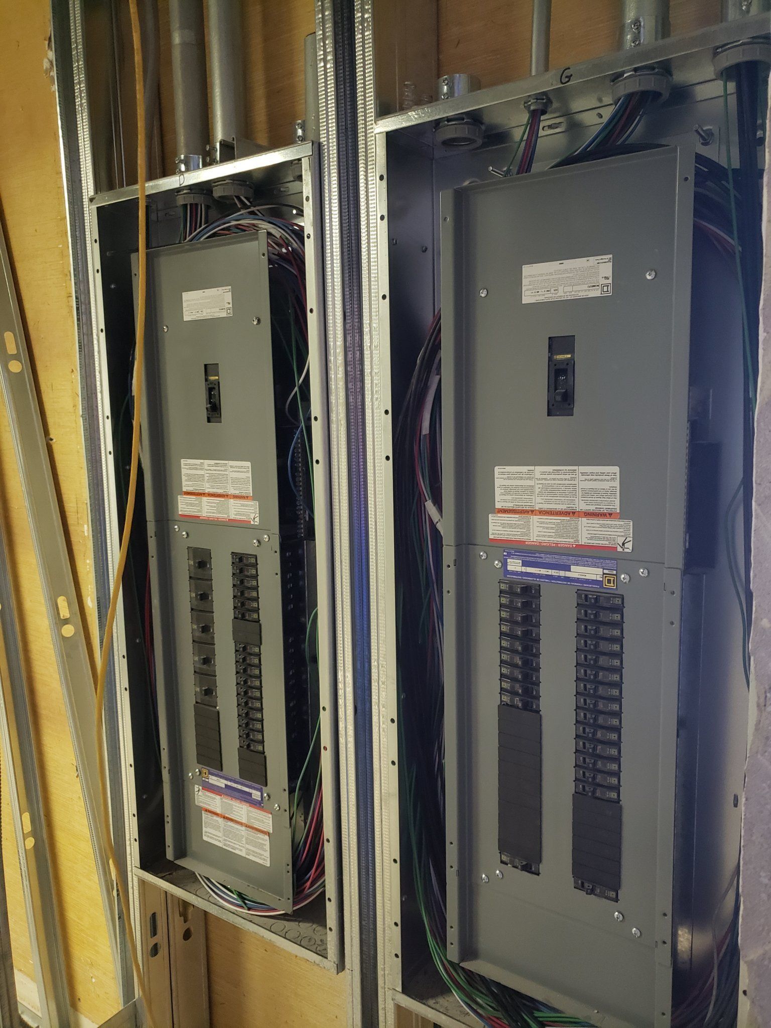 Two electrical panels installed in a wall frame with wires and conduit.