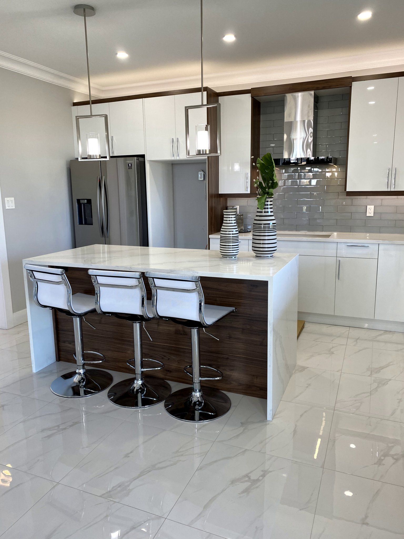 Modern kitchen with white cabinets, island with stools, stainless steel appliances, and tiled floor.