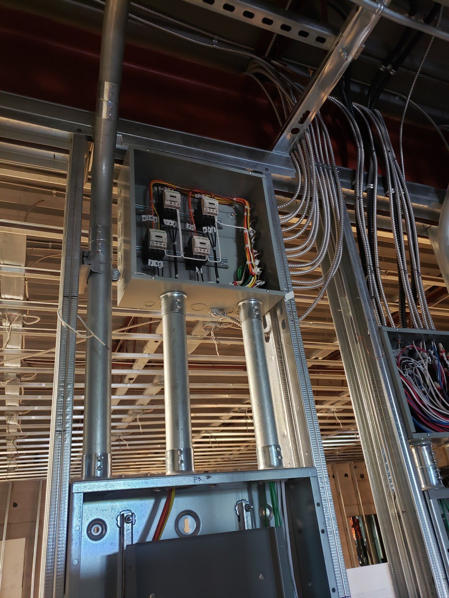 Electrical wiring installation in building ceiling. Metal boxes, conduits, and cables visible.