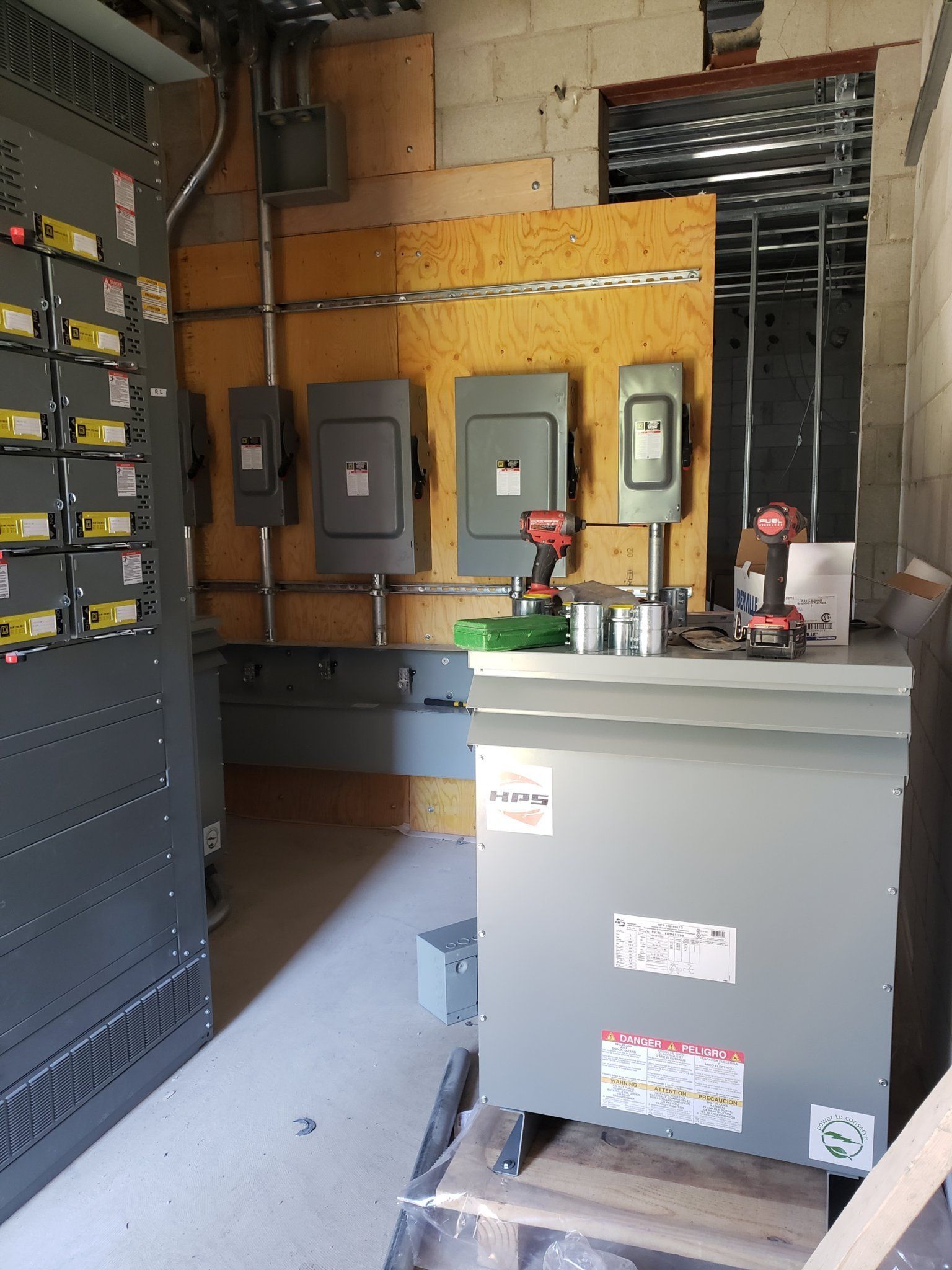 Electrical room with gray panels, transformer, wiring, and construction tools.