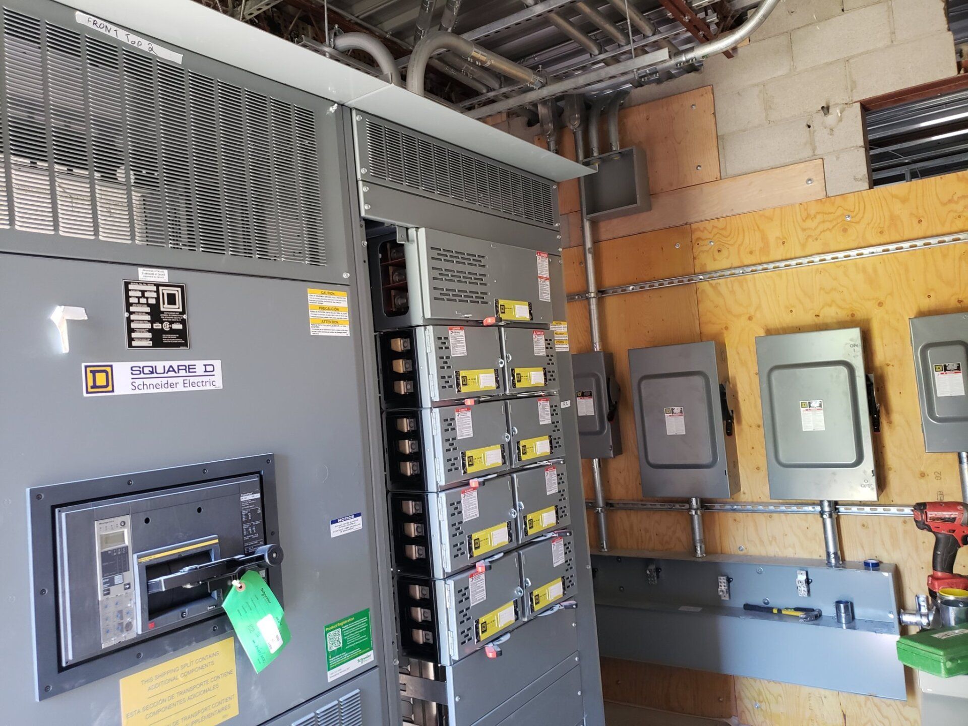 Electrical panel with circuit breakers, conduit, and several gray metal boxes mounted on a wood wall.