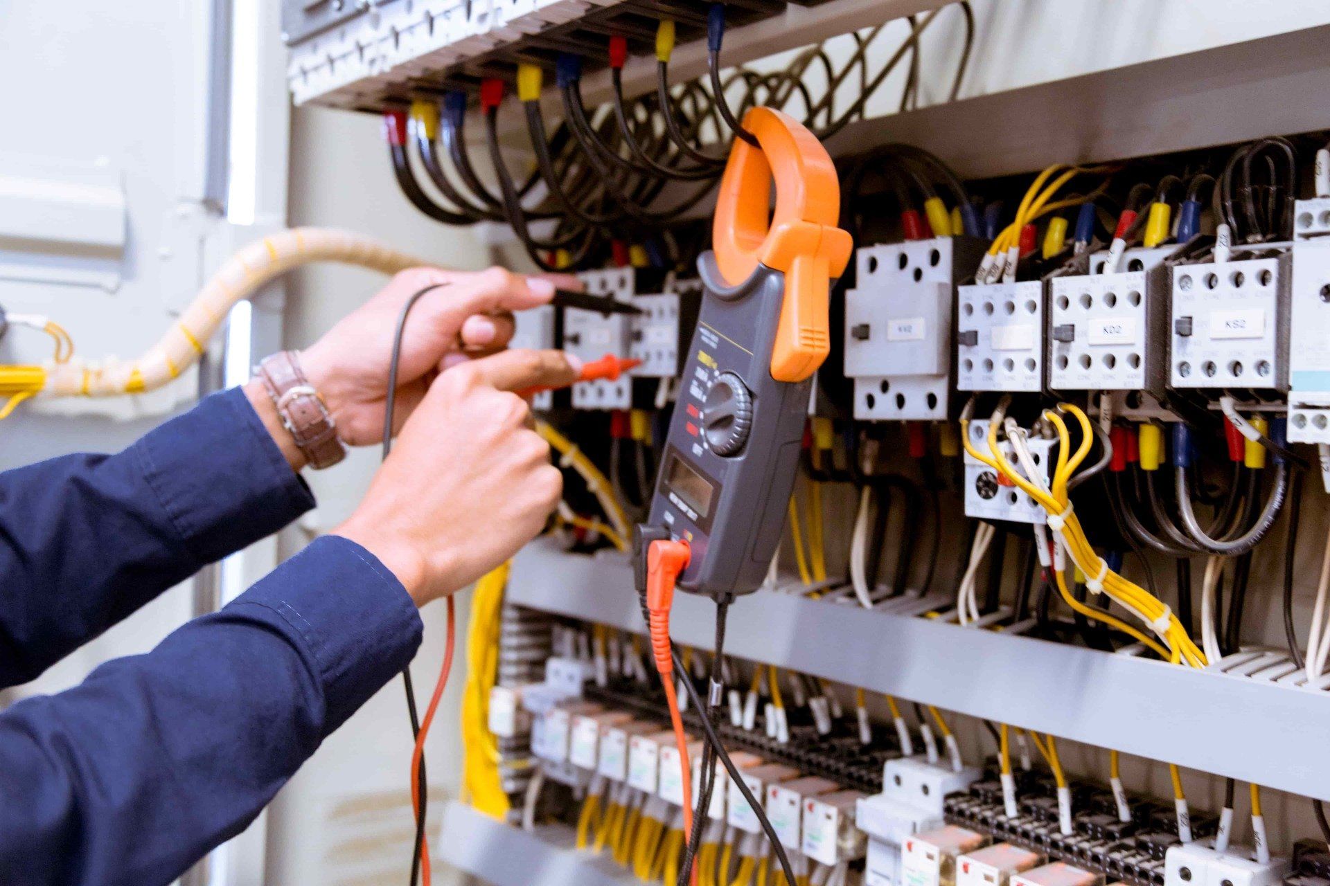 Electrician using a clamp meter to test wires in an electrical panel.