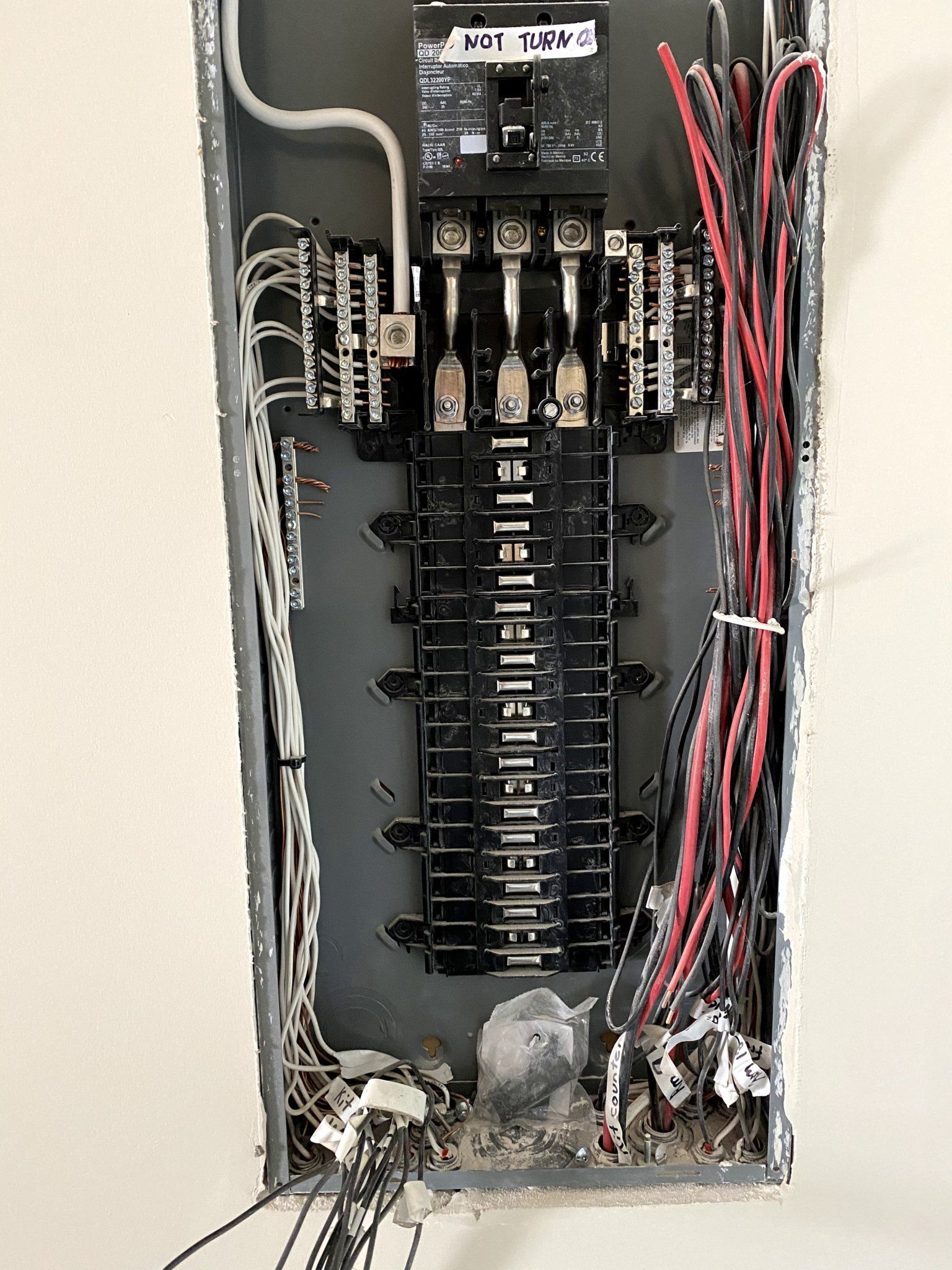 Electrical panel with various wires, mostly black and red, exposed inside a metal enclosure.