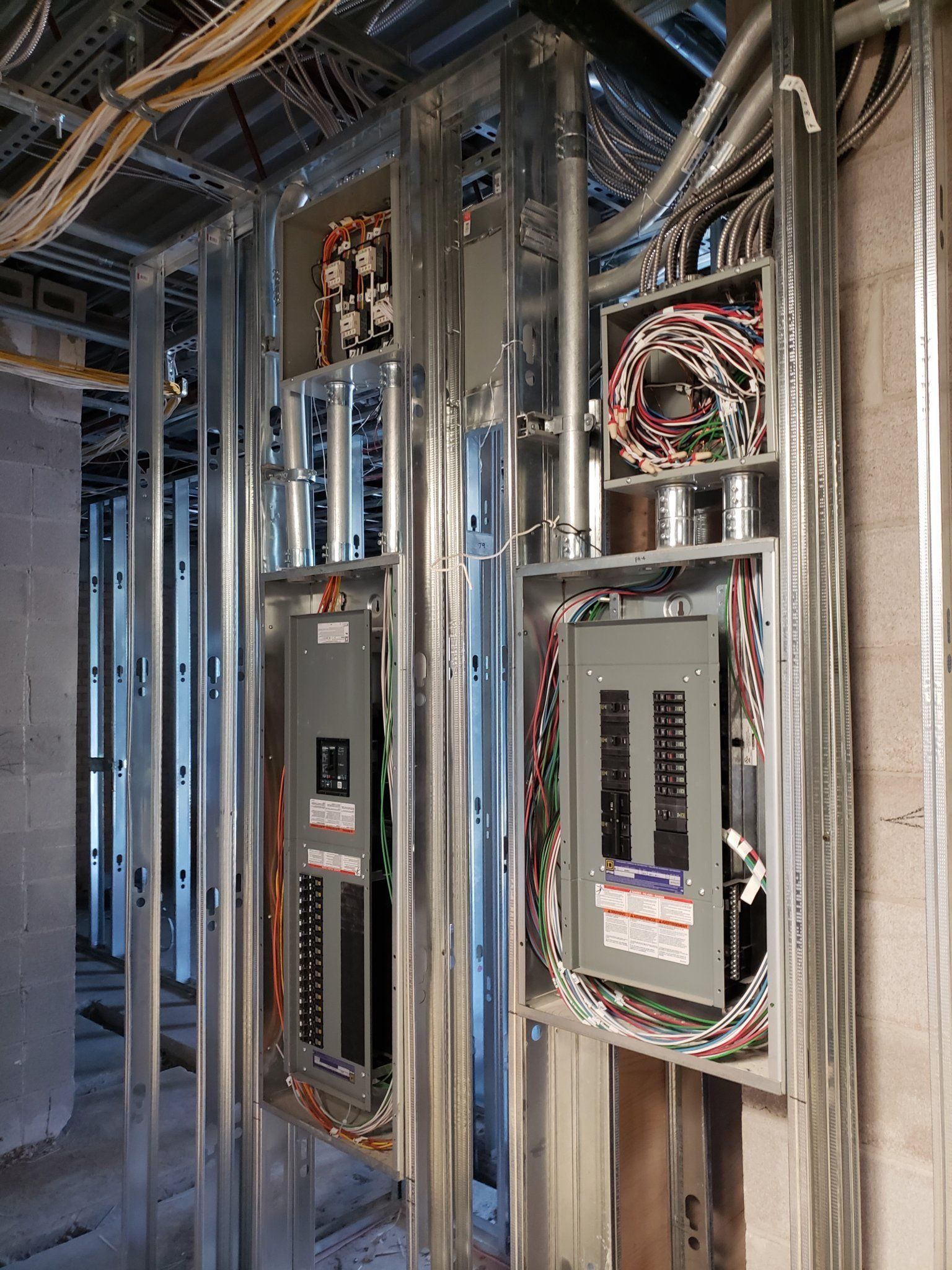 Electrical panels installed in metal framing within a building under construction, showing wiring and conduit.