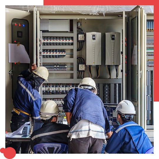 Electrical workers in safety gear inspect control panel.