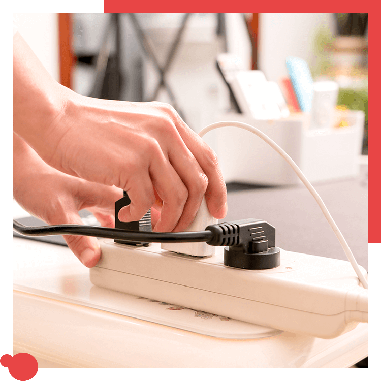 Hands plugging a black cord into a white power strip, with another white cord already connected.