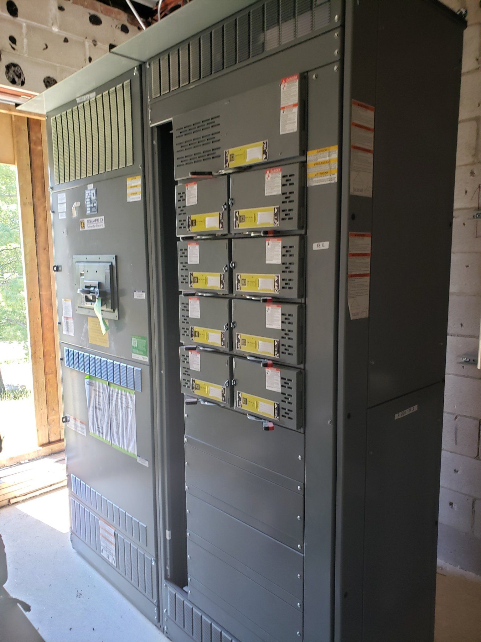 Large gray electrical panel with circuit breakers in a construction setting.