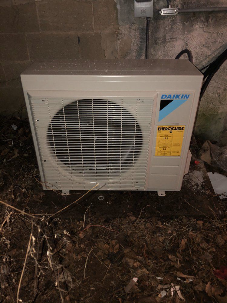 a daikin air conditioner is sitting on the ground next to a brick wall .
