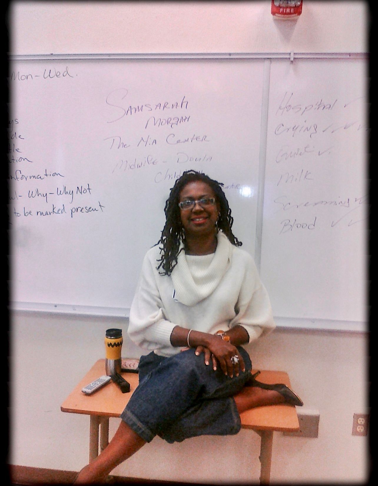 Woman Sits on a Desk in Front of a White Board