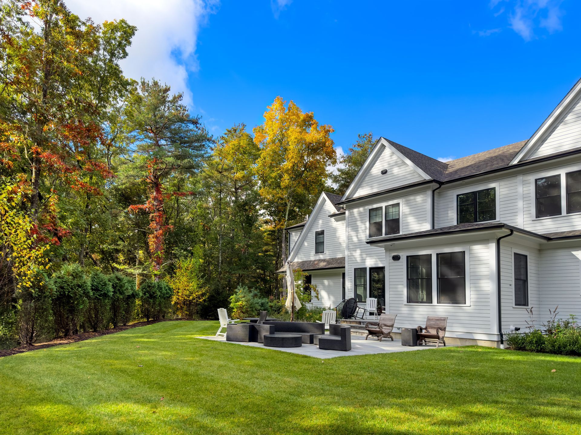 White house with a stone patio, lawn, and trees under a blue sky.