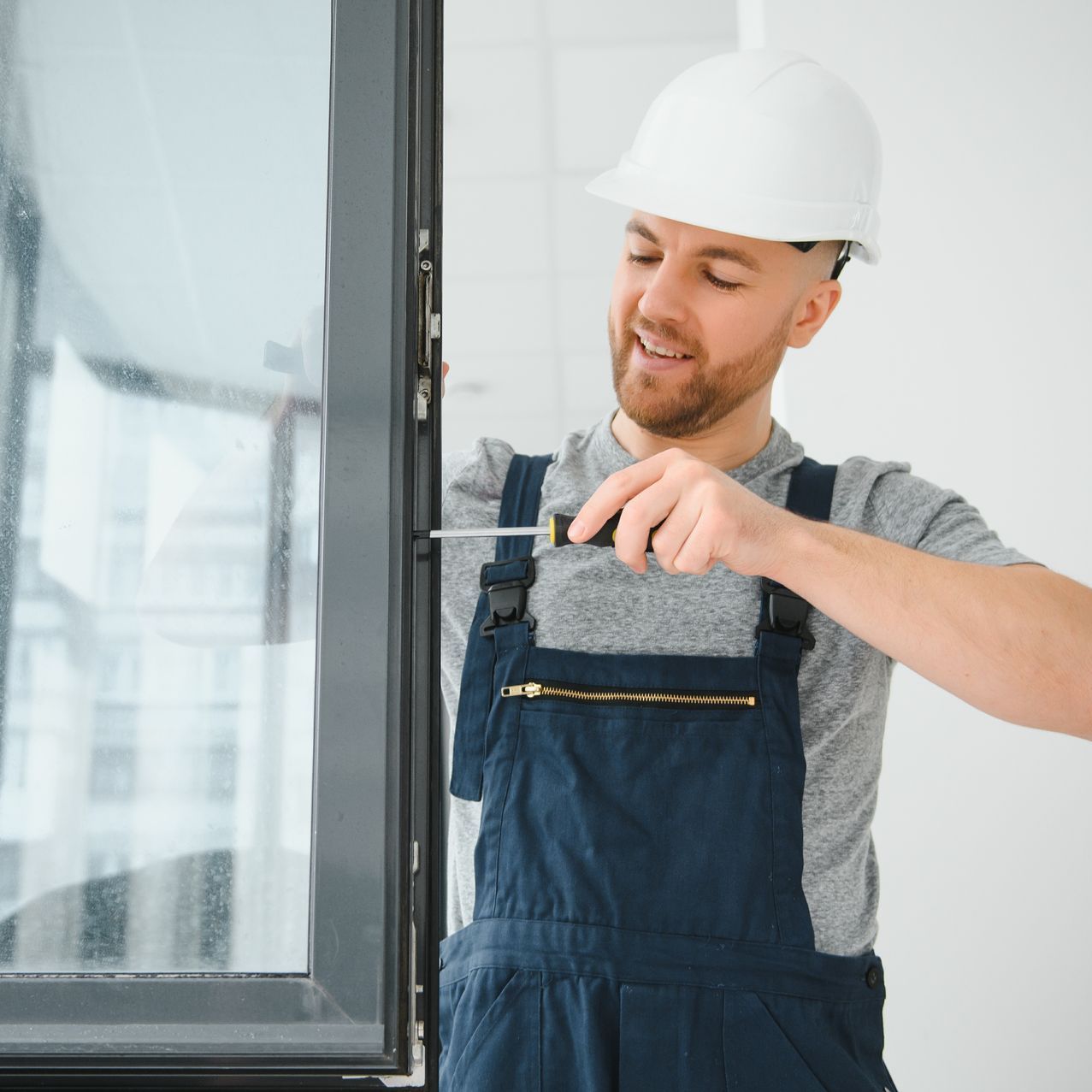 a man wearing overalls and a hard hat is working on a window .